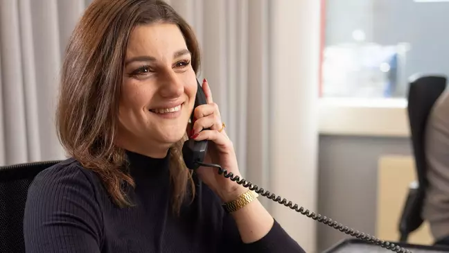 Egy nő telefonál, miközben a munkahelyén ül, és mosolyog