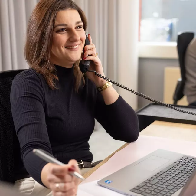 Egy nő telefonál, miközben a munkahelyén ül, és mosolyog