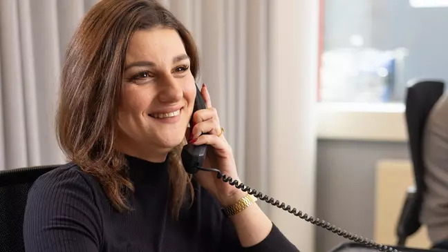 Egy nő telefonál, miközben a munkahelyén ül, és mosolyog
