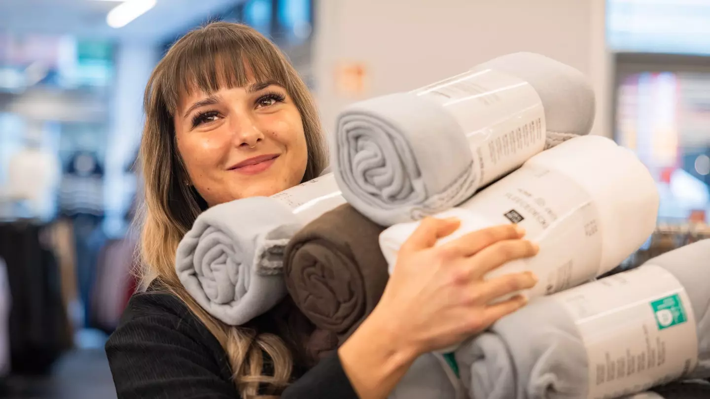 Egy nő mosolyogva áll egy üzletben, és rengeteg árut tart a kezében