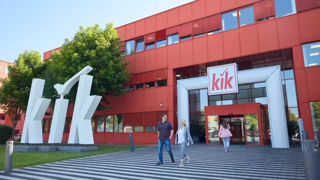 A KiK piros épülete, amelynek bejárata előtt egy nagy fehér logó látható, és több ember tart az épület felé.